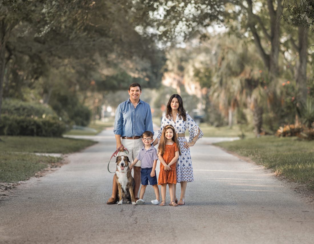 Family portrait with their dog on a tree-lined road