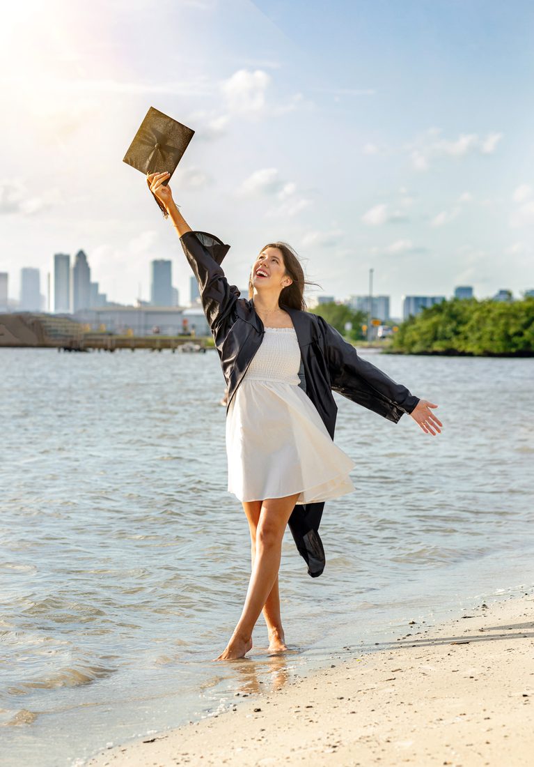 Senior portrait tossing a graduation cap on the beach